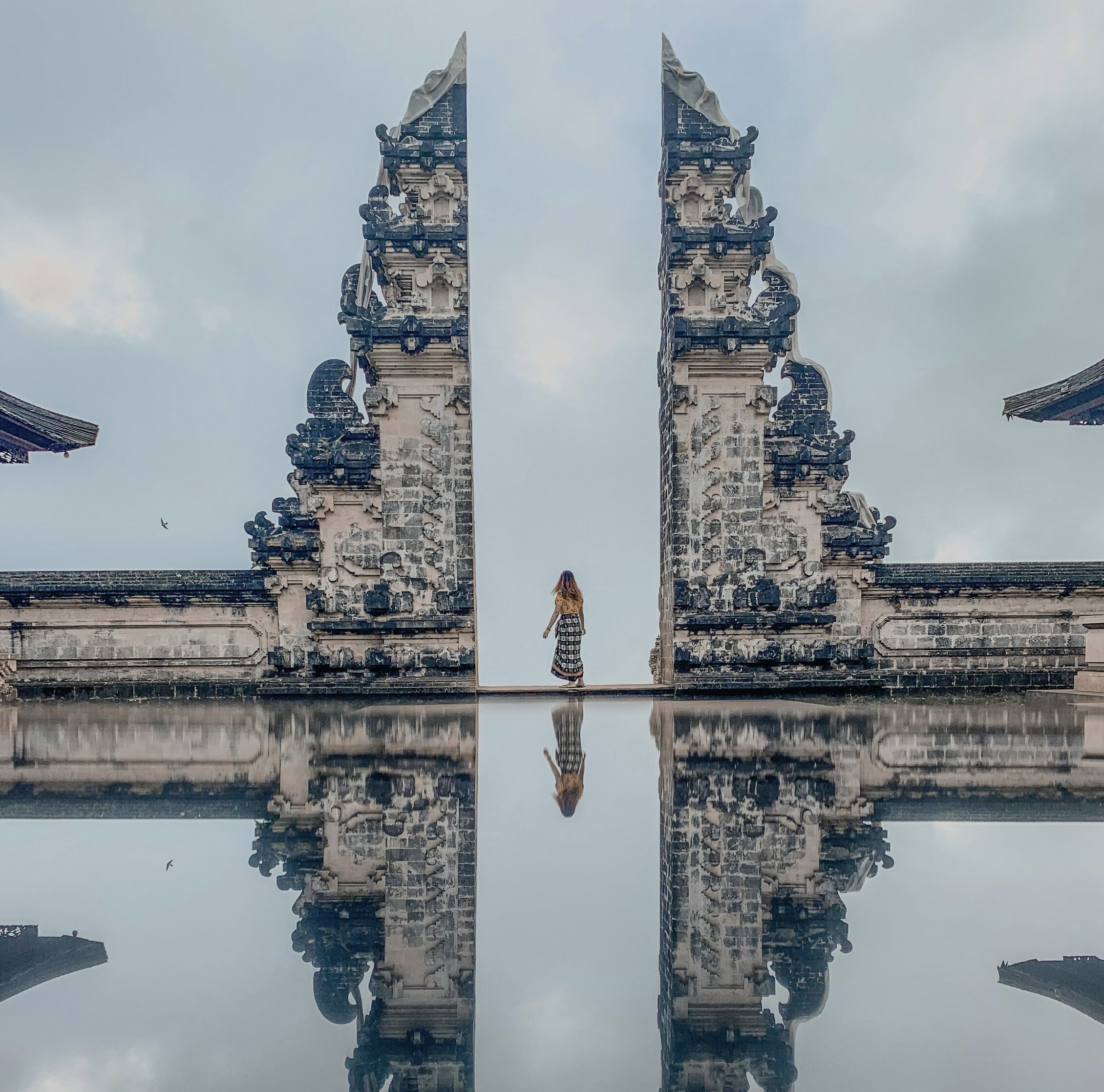 woman standing between concrete landmark in Bali with reflection in water